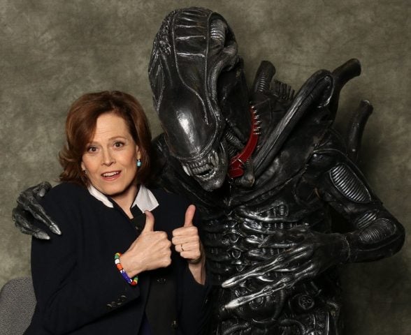 Sigourney Weaver posando con los pulgares levantados junto a un fan disfrazado de alien